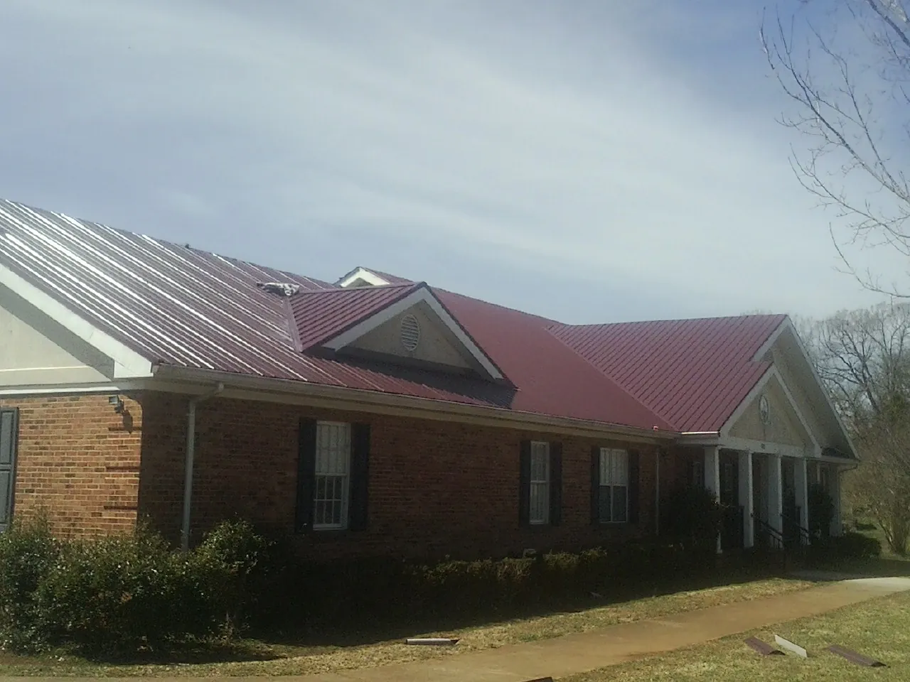 Red metal roof with gabled entries on a long brick building, from a Hail Damage Roof Repair job in Hickman