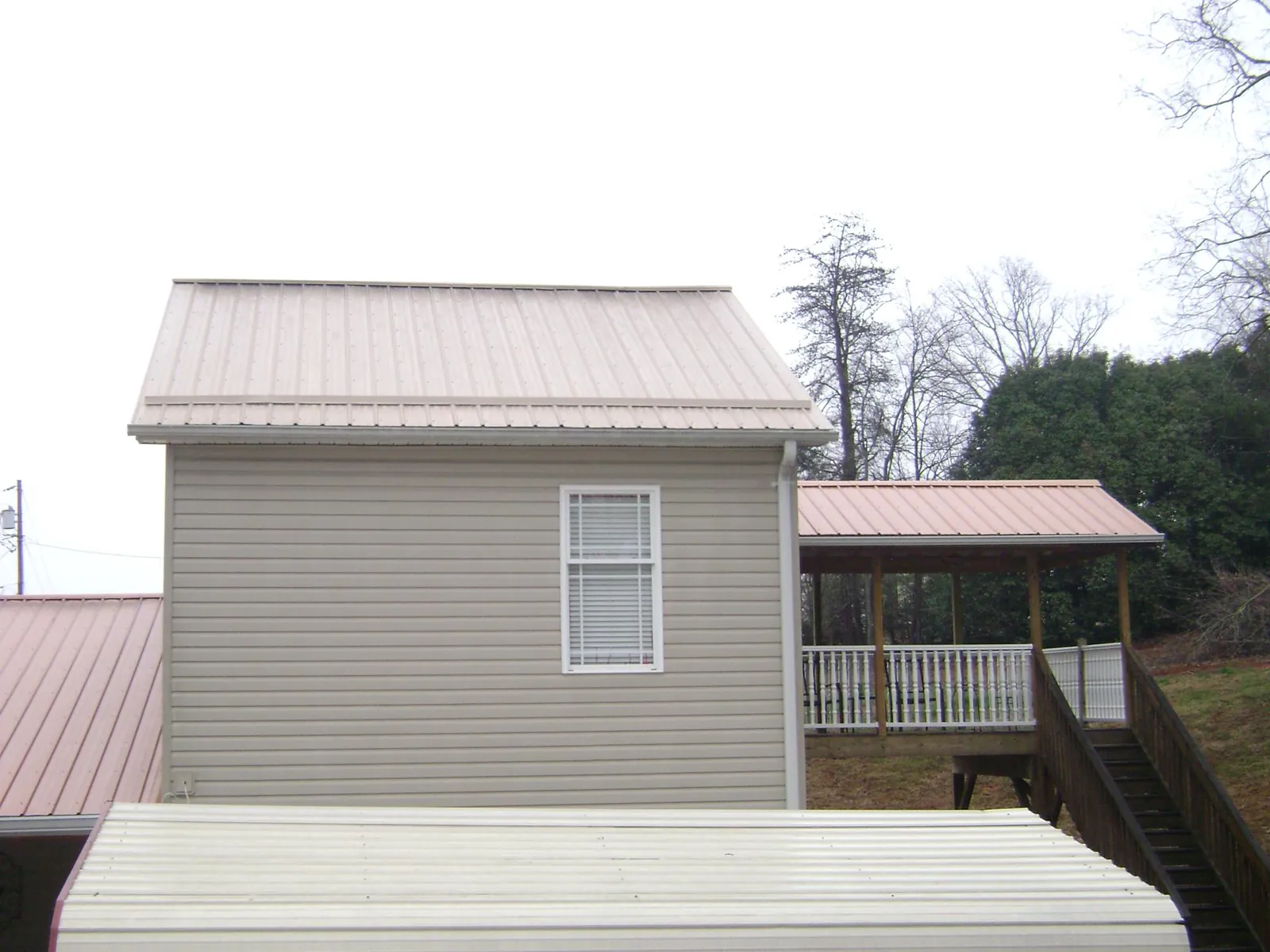 Tan metal roofs on a two story addition and attached porch, from a Roof Replacement job in Hickman